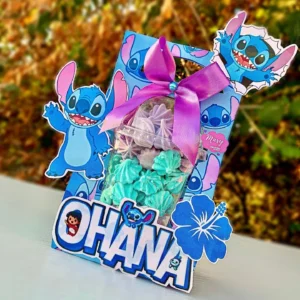 Embalagem alta com base quadrada em tom azul escuro com estampas tropicais de folhas de hibisco e o rosto sorridente do Stitch na frente, trazendo um visor circular vazado que exibe o espaço para o copo e alça superior em arquivo digital de corte.