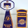 Topper de bolo esportivo exibindo uma quadra de basquete ao fundo com uma tabela oficial em acrílico fictício, trazendo uma grande bola alaranjada em destaque e silhuetas de atletas em posições de enterrada em camadas tridimensionais em arquivo digital de corte.