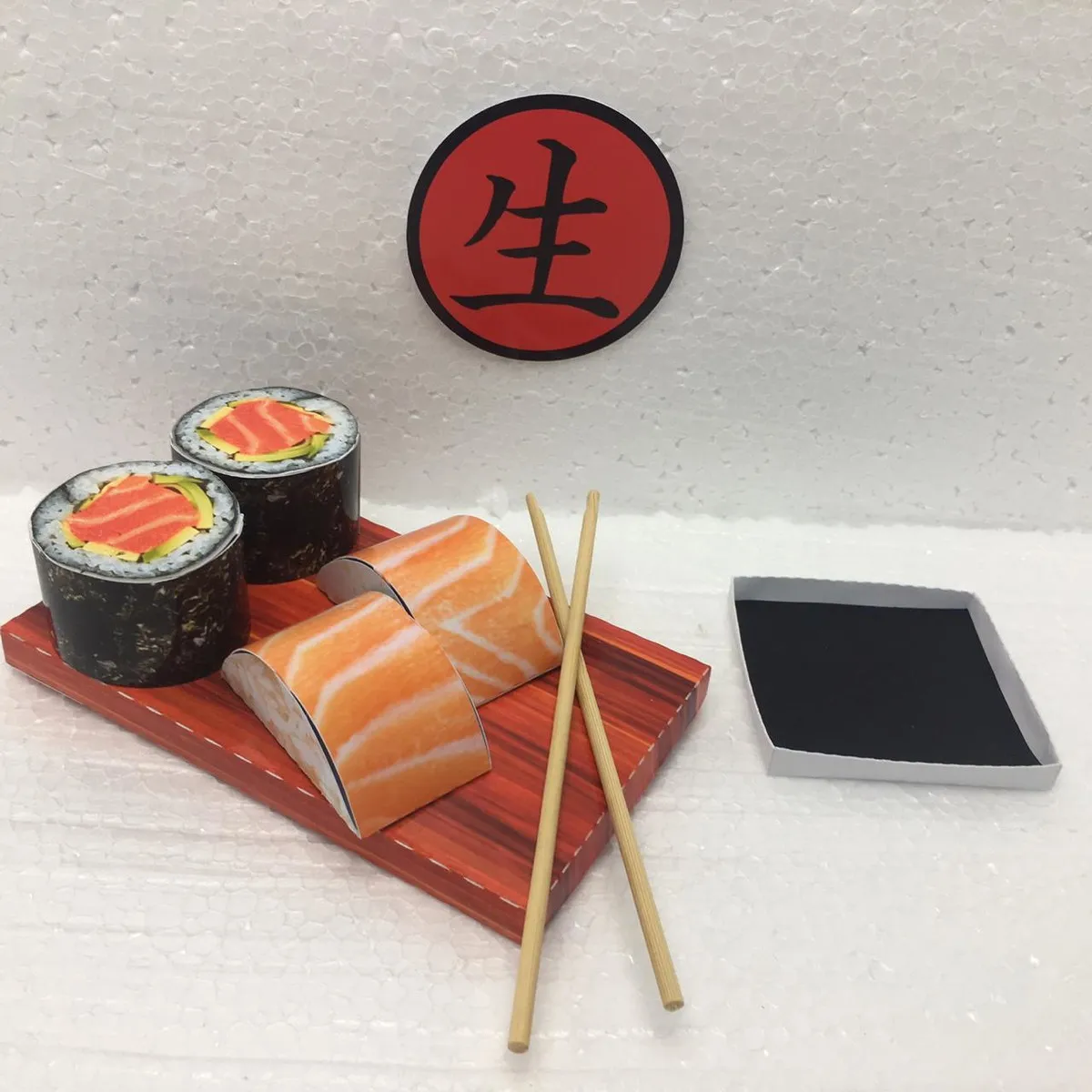 Topper de bolo criativo ilustrando peças de comida japonesa como uramakis, sushis com gergelim e temakis fofos com um par de hashis de madeira cruzados, dispostos em camadas tridimensionais em arquivo digital de corte.