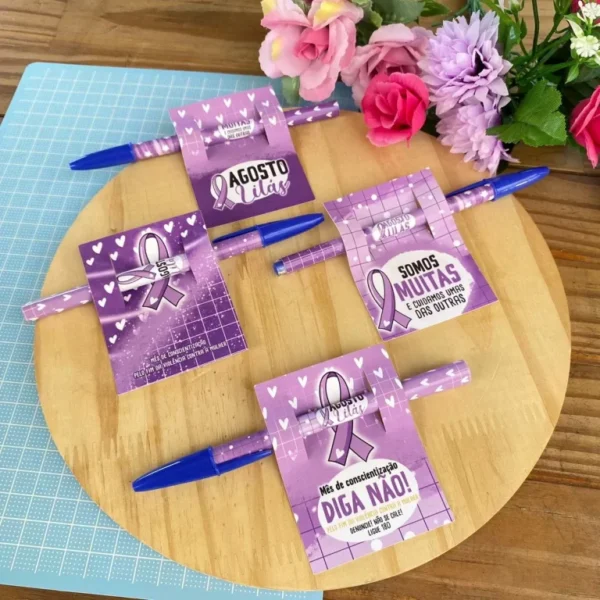 Molde digital de caixa quadrada de papel na cor lilás com visor transparente em formato de coração, exibindo ramos florais decorativos nas bordas e logotipo da campanha.