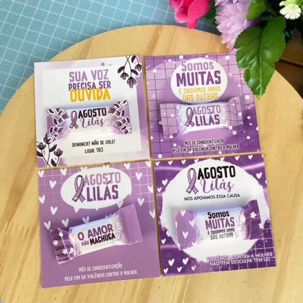 Cartão vertical lilás com estampa de laço da conscientização e marcas de corte paralelas na parte inferior para fixação de uma mini lixa de unha descartável.
