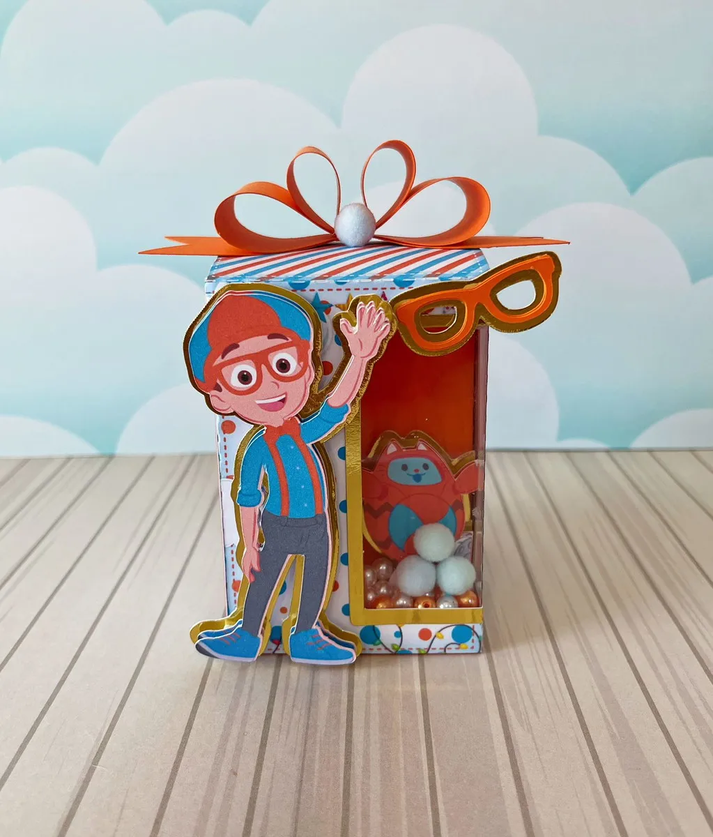 Embalagem em formato de maleta de ferramentas com alça superior reforçada, decorada com lupas e patinhas, trazendo o Blippi sorridente na frente em aplique tridimensional em arquivo digital de corte.