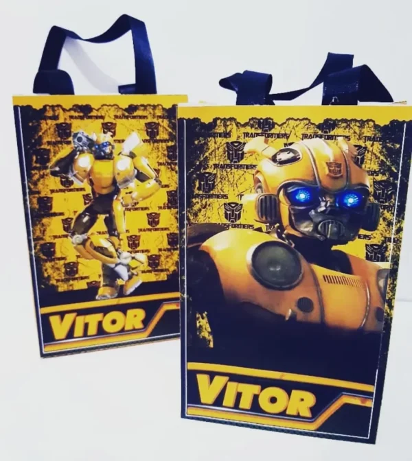 Elementos digitais para topo de bolo do Bumblebee, exibindo a silhueta de prédios escuros, raios amarelos ao fundo, faixa de nome estilizada e o herói em pose de ação.