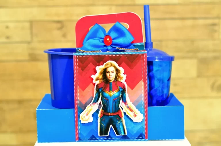 Elementos digitais para topo de bolo da Capitã Marvel exibindo a silhueta da heroína voando, raios de energia em neon e faixa amarela para personalização do nome.
