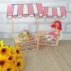 Molde de papel para imprimir simulando uma mini barraca de festa junina, com teto listrado de vermelho e branco, balcão de madeira e pequenas bandeiras presas.