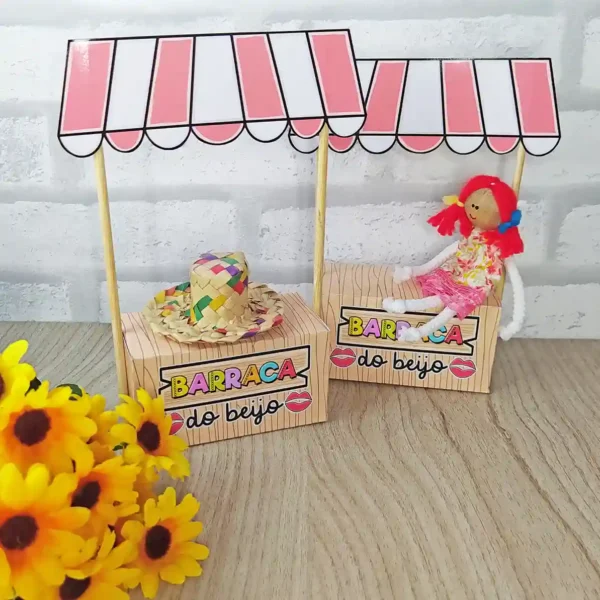 Molde de papel para imprimir simulando uma mini barraca de festa junina, com teto listrado de vermelho e branco, balcão de madeira e pequenas bandeiras presas.