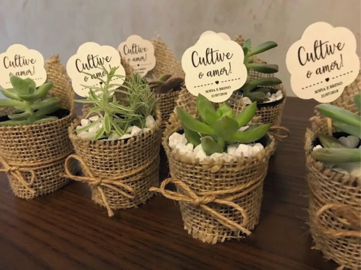 Tag de papel suspensa com formato geométrico e furo superior, exibindo a frase Cultive o Amor em lettering delicado ao lado de ilustrações de raminhos de plantas.