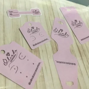 Tag de papel retangular com cantos arredondados na cor branca, exibindo furos exatos na parte superior para brincos e um vinco centralizado para dobras de colares, com acabamento limpo em camadas tridimensionais em arquivo digital de corte.