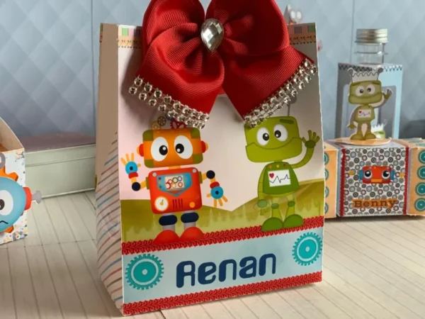 Elementos digitais para topo de bolo exibindo uma engrenagem gigante como fundo, um robô segurando uma placa de feliz aniversário e faixas para personalização.