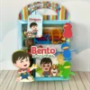 Centro de mesa com base sextavada amarela, trazendo no topo o cãozinho Totó e o menino Bento dentro da cesta de um grande balão de ar quente colorido que parece flutuar entre nuvens em camadas tridimensionais em arquivo digital de corte.