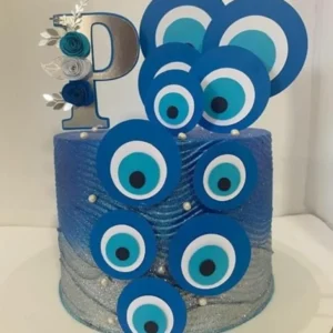 Elementos digitais para topo de bolo com o tema Olho Grego, exibindo mandalas circulares concêntricas nas cores azul-escuro, azul-claro e branco, com detalhes dourados em filigrana e ramos de folhas metálicas.