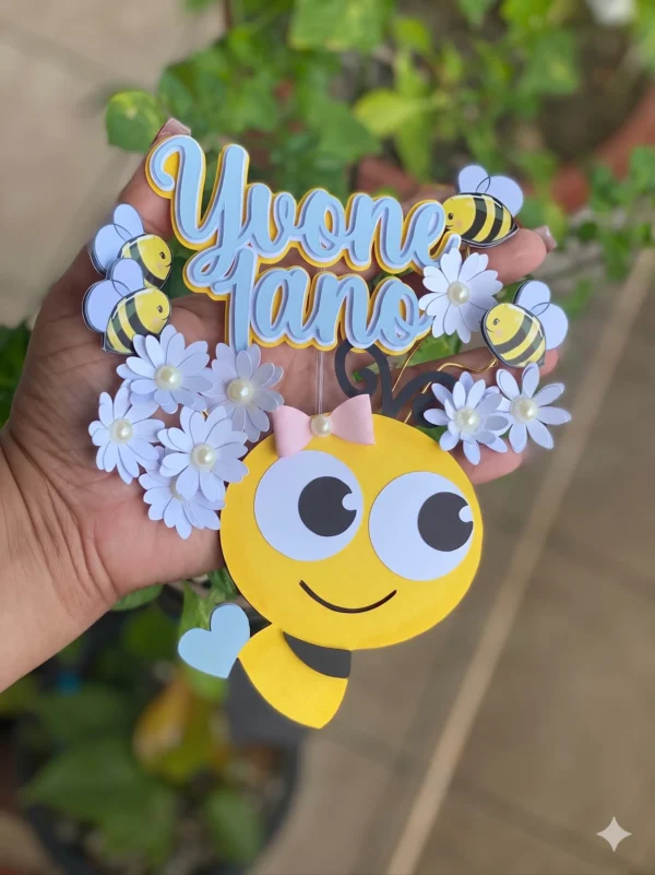 Topper de bolo infantil com uma colmeia amarela texturada em formato de gota ao centro, cercada por pequenas abelhinhas fofas com asas brancas e flores de margarida detalhadas com miolo amarelo dispostas em camadas tridimensionais em arquivo digital de corte.