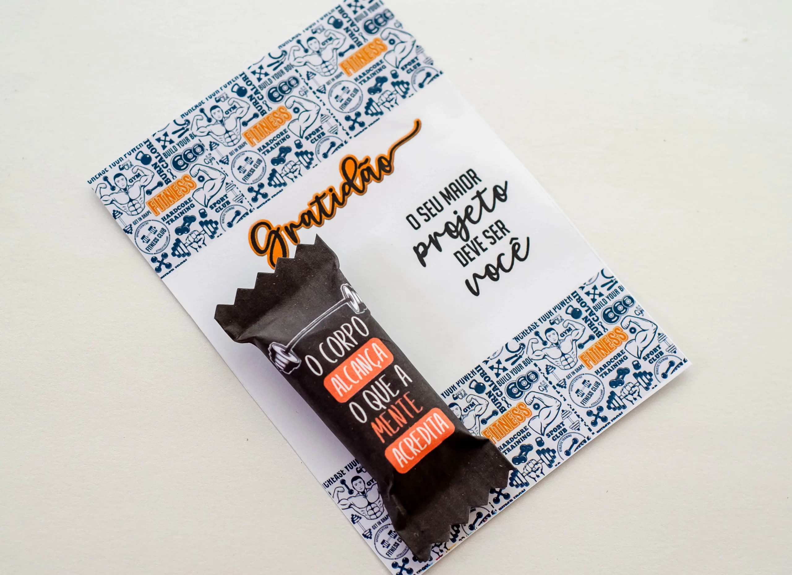 Kit digital com artes para encapar balas com desenhos de halteres, shakes e frases motivacionais como "foco no treino" dispostos em folha pronta para impressão.