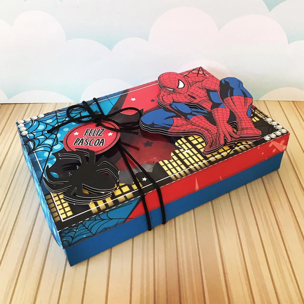 Tampa de caixa cenário com o Homem-Aranha saltando entre prédios em papelaria de camadas para kit interativo de confeitaria infantil.