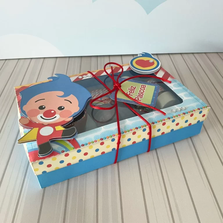 Caixa cartonada para doce mini confeiteiro decorada com o palhaço Plim Plim segurando notas musicais, clave de sol amarela na tampa e fundo azul com estrelas brilhantes em arquivo digital de corte.