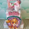 Topper de bolo com a cadelinha Skye voando em seu helicóptero e detalhes de patinhas e ossos em camadas tridimensionais rosa para decoração de festas.