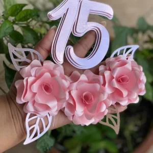 Topper de bolo de debutante com o número 15 recortado em letras elegantes com brilho dourado, cercado por arranjos de rosas abertas em tons de rosa e delicados ramos de folhagens dispostos em camadas tridimensionais em arquivo digital de corte.