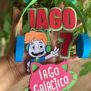 Topper de bolo em camadas com o tema do Gato Galáctico, exibindo o personagem de capuz azul, estrelas sorridentes, foguetes coloridos e uma faixa central amarela para nome.