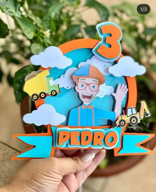 Topper de bolo infantil com o personagem Blippi acenando alegremente vestindo seu boné azul e laranja, óculos e gravata borboleta brilhantes, cercado por um trator e estrelas coloridas dispostos em camadas tridimensionais em arquivo digital de corte.