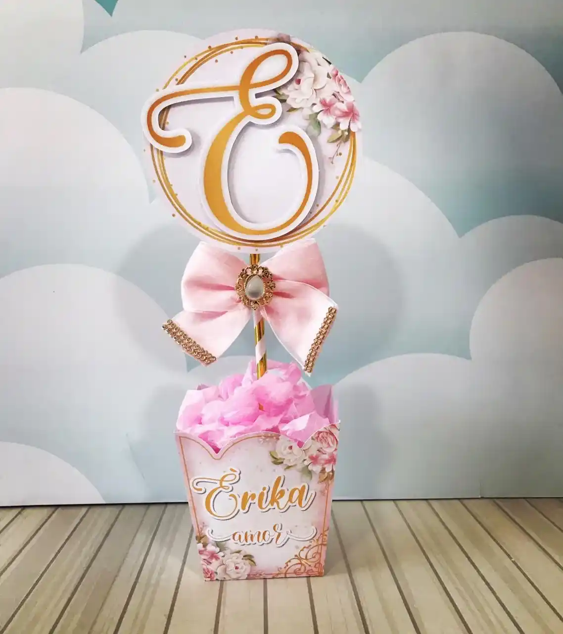 Mockup digital de um topo de bolo montado com flores rosas tridimensionais, destacando a textura das pétalas e o brilho dos ramos de folhas intercalados, com uma fonte elegante para o nome da aniversariante.