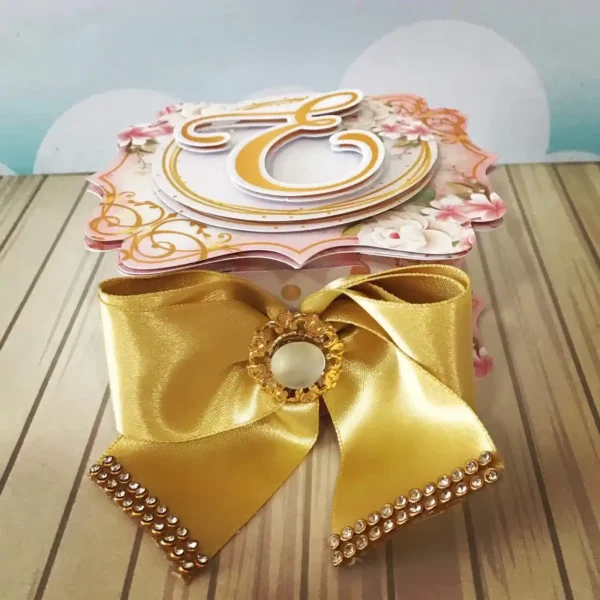 Design digital de topo de bolo para aniversário feminino exibindo flores rosas em 3D, ramos de folhas em papel lamicote dourado e molduras para nome, estruturado para montagem em camadas sobrepostas para efeito de profundidade.