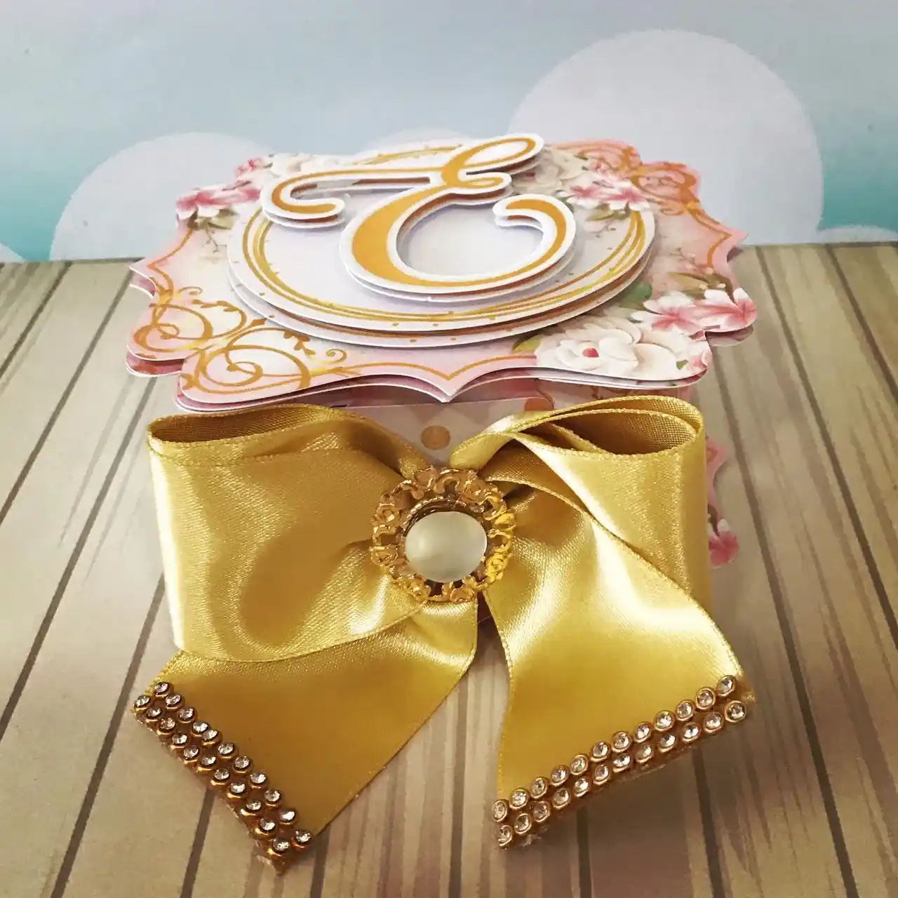 Design digital de topo de bolo para aniversário feminino exibindo flores rosas em 3D, ramos de folhas em papel lamicote dourado e molduras para nome, estruturado para montagem em camadas sobrepostas para efeito de profundidade.