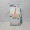 Mockup digital de um topo de bolo montado com o tema Unicórnio, destacando o chifre e orelhas em relevo com apliques de papel dourado e detalhes florais em camadas sobrepostas.