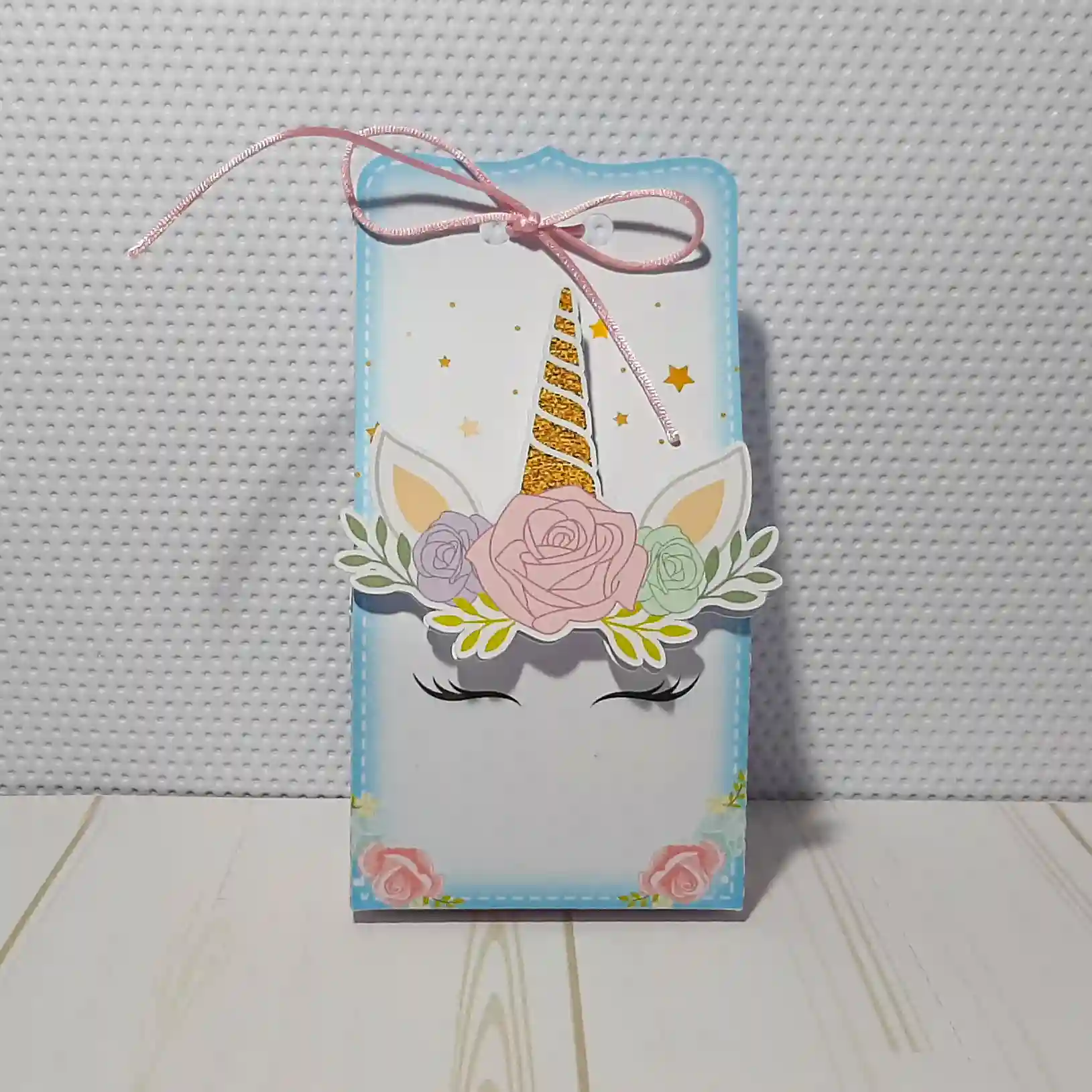 Mockup digital de um topo de bolo montado com o tema Unicórnio, destacando o chifre e orelhas em relevo com apliques de papel dourado e detalhes florais em camadas sobrepostas.