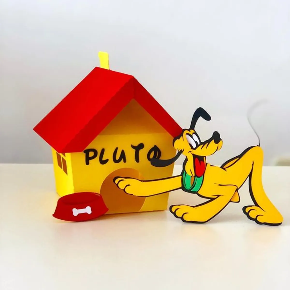 rquivo de corte digital de topo de bolo no tema Pluto em formato Studio para Silhouette, mostrando o clássico cãozinho sorridente e com a língua para fora, acompanhado por ossinhos, pegadas, sua casinha de cachorro e balões coloridos dispostos em camadas prontas para recorte tridimensional.