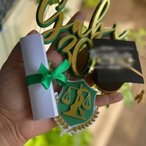 Arquivo de corte digital de topo de bolo para Formatura de Nutrição em formato Studio para Silhouette, mostrando o símbolo da nutrição com a balança e a serpente, um capelo de formatura, diploma amarrado com fita verde e elementos florais dispostos em camadas prontas para recorte tridimensional.